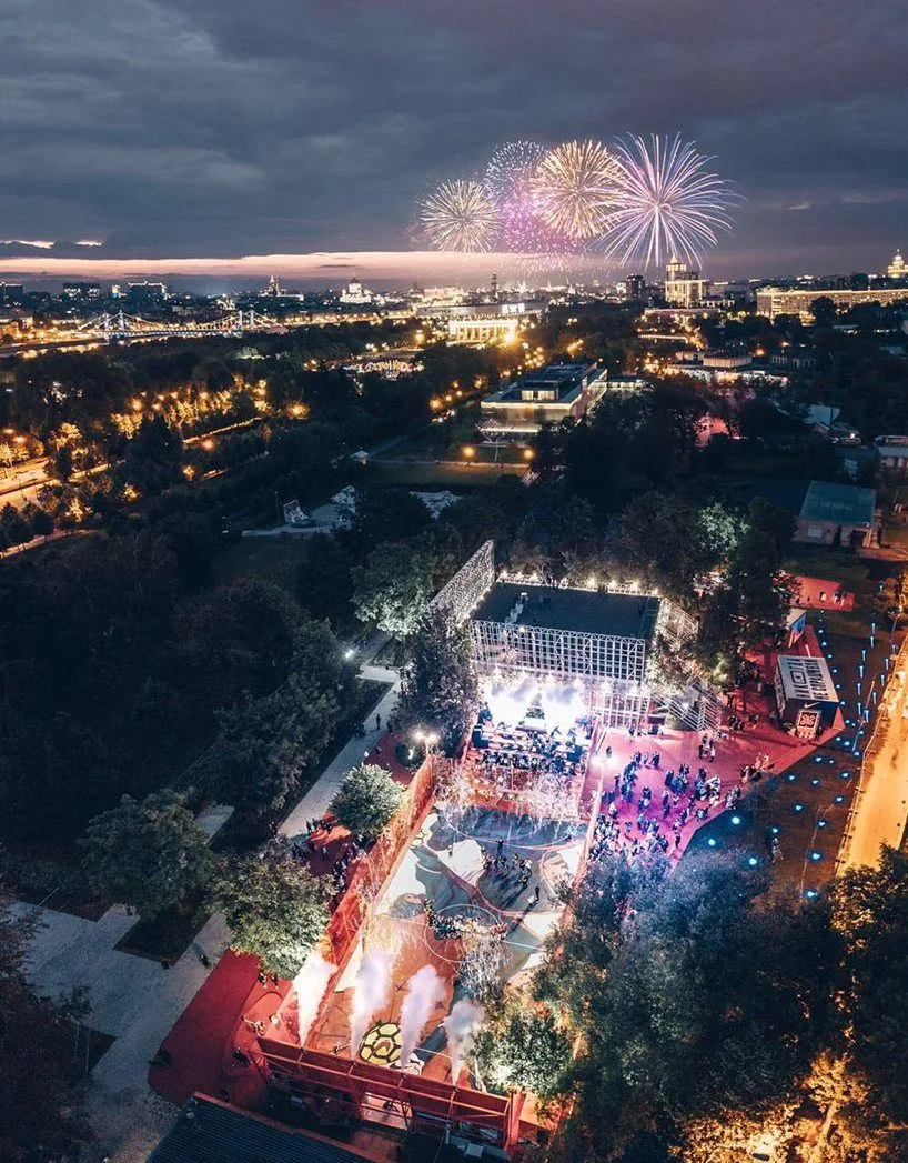 Aerial night view of Nike Box MSK in Moscow's Gorky Park: a lit football pitch and pavilion packed with people, fireworks over the city skyline
