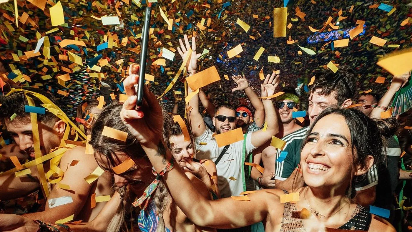 Young partygoers smiling and cheering under a shower of colorful confetti at an elrow event